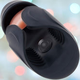 A close-up of a black cylindrical object, possibly a Zero Tolerance Lick the Tip male masturbator, featuring a textured interior and smooth exterior against a blurry background with pastel-colored lights.